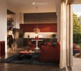 Modern living room with a sofa, coffee table, chairs, a kitchen area with cabinets and a kitchen island, pendant light, large screen, vases, and picture frames. The room has wooden flooring and large windows with a view of the city.