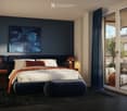 Modern bedroom with a large bed, nightstands, lamps, a stool, and a painting on the wall. The room features dark blue walls, a dark wooden floor, and a large window with a view of a balcony.