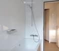 Modern bathroom with a white bathtub, a handheld showerhead, a towel rack, and white tiled walls.