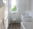 Modern bathroom with white tiles, a toilet, a bathtub, a sink with a faucet, a mirror, and a radiator.