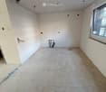 Empty room with bare walls and unfinished concrete floor, featuring a window on one side and exposed electrical wiring and plumbing.