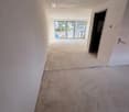 Empty room with unfinished concrete floor and white walls, featuring a doorway leading to an outdoor area with glass doors.