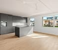 Modern kitchen with grey cabinets, a central island, and large windows overlooking a garden area.