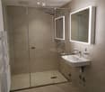 Modern bathroom with a glass-enclosed shower, a white sink with a modern faucet, and illuminated mirrors on the wall.