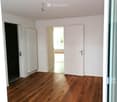 Empty room with wooden flooring, white walls, and a radiator on one wall. There are two doors, one leading to another room and the other to an outdoor area.