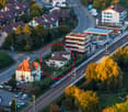 Aerial view of a residential area with multiple houses, a train station, a gas station, and surrounding greenery.