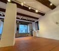 Empty room with exposed wooden beams, terracotta tiled floor, white walls, and large windows offering a view of the outside.