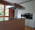 Modern kitchen with stainless steel appliances, wooden cabinets, and a large window overlooking greenery.