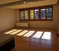 Empty room with wooden flooring, large windows with wooden frames, radiator, and natural light streaming in.