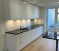 Modern kitchen with white cabinets, dark countertops, a sink, and a small black table near the window.
