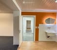 Modern hallway with wooden flooring, white walls, and a sink area visible in the background.