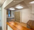 Modern, minimalist hallway with wooden flooring, built-in wooden cabinetry, and a small bench. Features recessed lighting and a glass door leading to another room.