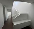 Modern hallway with white walls, wooden flooring, and a staircase leading upwards. The hallway features built-in storage units and a neutral color palette.