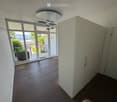 Empty room with wooden flooring, large glass sliding doors leading to a balcony with a scenic view, white built-in wardrobes, and a modern ceiling light fixture.