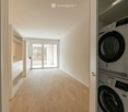 Empty hallway with wooden flooring, white walls, and a large glass door leading to an outdoor area. Laundry area visible with stacked washer and dryer.