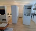 Modern, compact living space with a sofa, small table, kitchen area, and built-in bed. Features white cabinets, a sink, and a small screen.