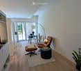 Modern living room with wooden flooring, a round coffee table, a sofa, a floor lamp, and a dining area visible through an open doorway.