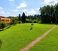 A large, well-maintained green lawn with a pathway leading to a building, surrounded by trees and shrubs under a partly cloudy sky.