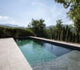 Outdoor swimming pool, surrounded by trees, mountains in the background, clear blue sky