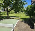 A well-maintained garden with a large lawn, trees, benches, and a ping pong table on a paved area.