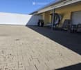 Terrace with brick pavement, covered area, sun loungers, umbrella, grill, table, and chairs.