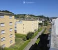 Multi-story residential building with yellow facade, multiple windows, balconies, and surrounding greenery.