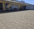 Brick-paved outdoor area with a sun lounger, table, chairs, and storage cabinet near a covered patio.