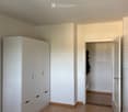 A modern, minimalistic bedroom with a blue bedspread, white wardrobe, and wooden flooring.
