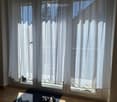 Empty room with large sliding glass door and white curtains, wooden floor, and a small rug near the door.