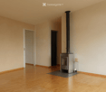 Empty room with wooden flooring, white walls, and a fireplace in the corner.