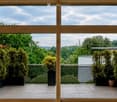 Spacious balcony with tiled floor, large windows, potted plants, and a view of a green landscape.
