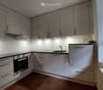 Modern kitchen with light grey cabinets, stainless steel appliances, and a black countertop.