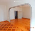 Empty room with wooden flooring and white walls, featuring an arched doorway leading to another room.