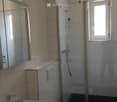 Modern bathroom with a sink, mirror, toilet, and a glass-enclosed shower with a window. Light-colored tiles and a sleek design.