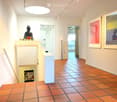A modern hallway with terracotta tiled flooring, white walls, and framed artwork. Features a small altar with a Buddha statue and candles, and a recessed ceiling light.