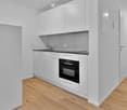 Modern kitchen with white cabinets, black countertop, and wooden flooring.