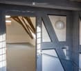 Room with wooden floor, wooden beams, white walls, open door, small window, carpet, chandelier, wall lamp