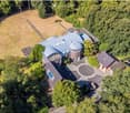 Aerial view of a large, modern house with a unique, curved roof design and multiple sections, surrounded by a well-maintained lawn and trees.