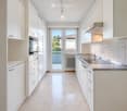 Modern kitchen with white cabinets, stainless steel sink, built-in oven, and a view of a balcony through a glass door.
