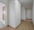Empty hallway with light wooden flooring, white walls, and several doors leading to other rooms.