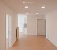 Empty hallway with light wooden flooring, white walls, recessed ceiling lights, and doors leading to adjacent rooms.