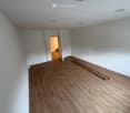 Empty room with light wooden flooring and white walls, featuring a doorway leading to another room.