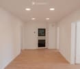 Empty hallway with light-colored walls, wooden flooring, and several doors including a main entrance door with a glass panel.