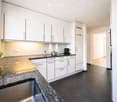 Modern kitchen with white cabinets, granite countertops, stainless steel sink, and various appliances including a coffee maker and a pot on the counter.