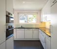 Modern kitchen with white cabinets, stainless steel oven, sink, and a window overlooking a balcony.