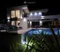 Modern two-story house with a swimming pool, lounge chairs, and outdoor seating area illuminated at night.