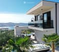 Modern house with a spacious outdoor area featuring a hot tub, dining table, chairs, and a view of the sea and mountains.