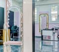 A modern, well-lit salon with a sleek design. Features include a large mirror, a stylish chair, a small table, and decorative floral arrangements.