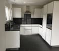Modern kitchen with white cabinets, black countertops, and black tiled flooring. Features a stainless steel range hood, sink, and oven.