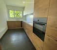 Modern kitchen with light wooden cabinets, stainless steel oven, dark tiled floor, and white countertops.